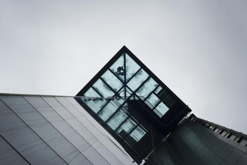 The image shows a modern building with a glass facade and a pointed roof, set against a gray sky. The building's design is...